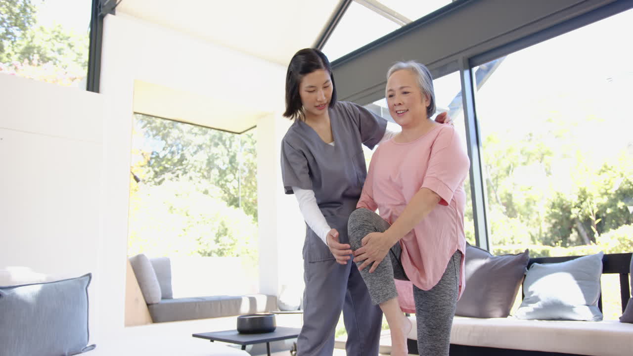 Physical therapist assisting senior asian woman with leg exercises at home