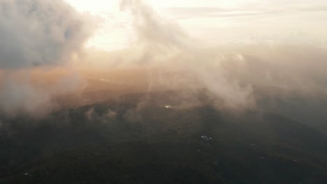 Aerial-view-flying-through-light-wispy-clouds-in-golden-light-at-sunset,-sunrise