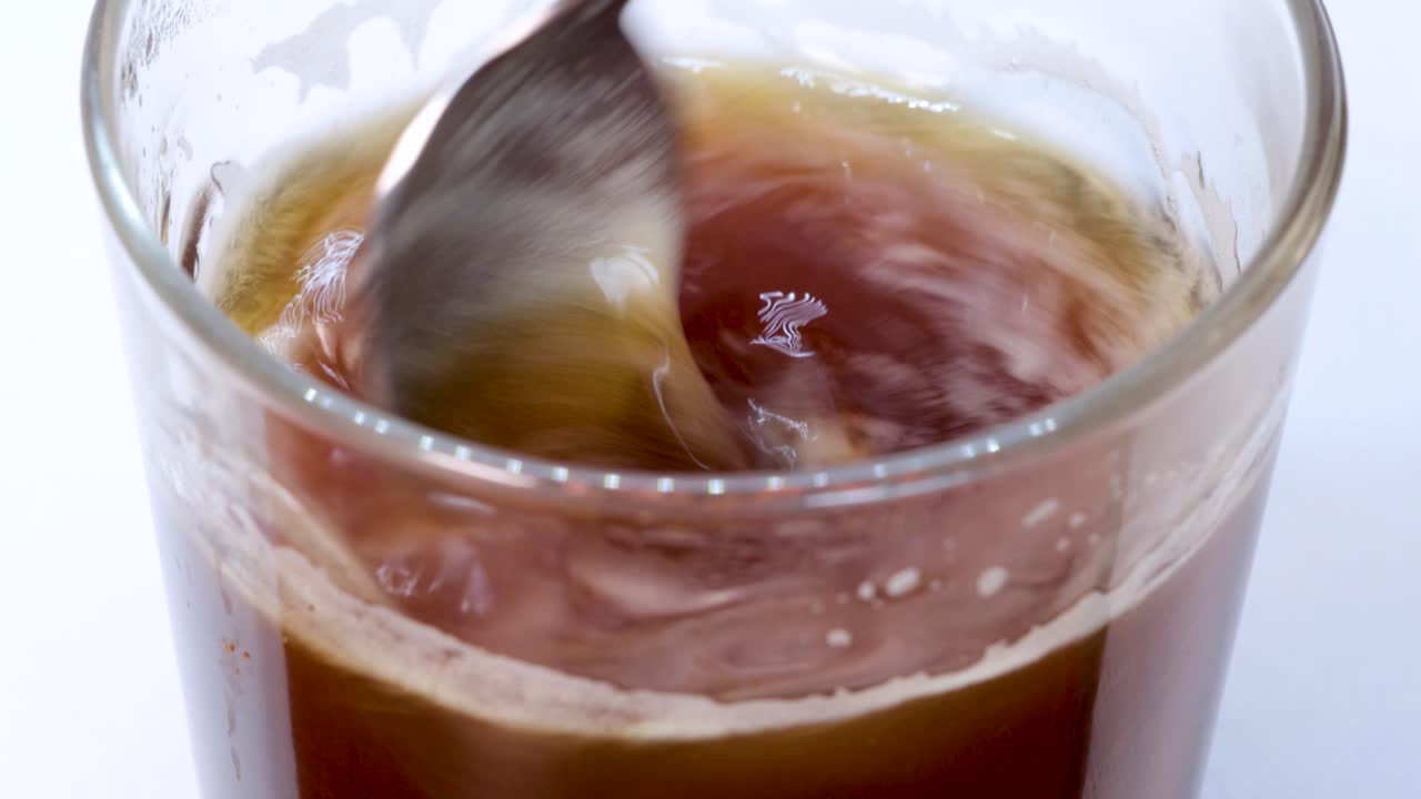 Vortice di caffè creato da un cucchiaio in un bicchiere trasparente, sfondo bianco