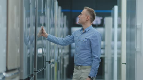 el hombre abre la puerta del refrigerador en la tienda de electrodomésticos y compara con otros modelos para comprar la nueva casa