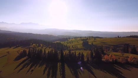 Toma-Aérea-De-Impresionantes-Paisajes-Montañosos,-Campos-Verdes,-Largas-Sombras,-Bosques-Y-Puesta-De-Sol