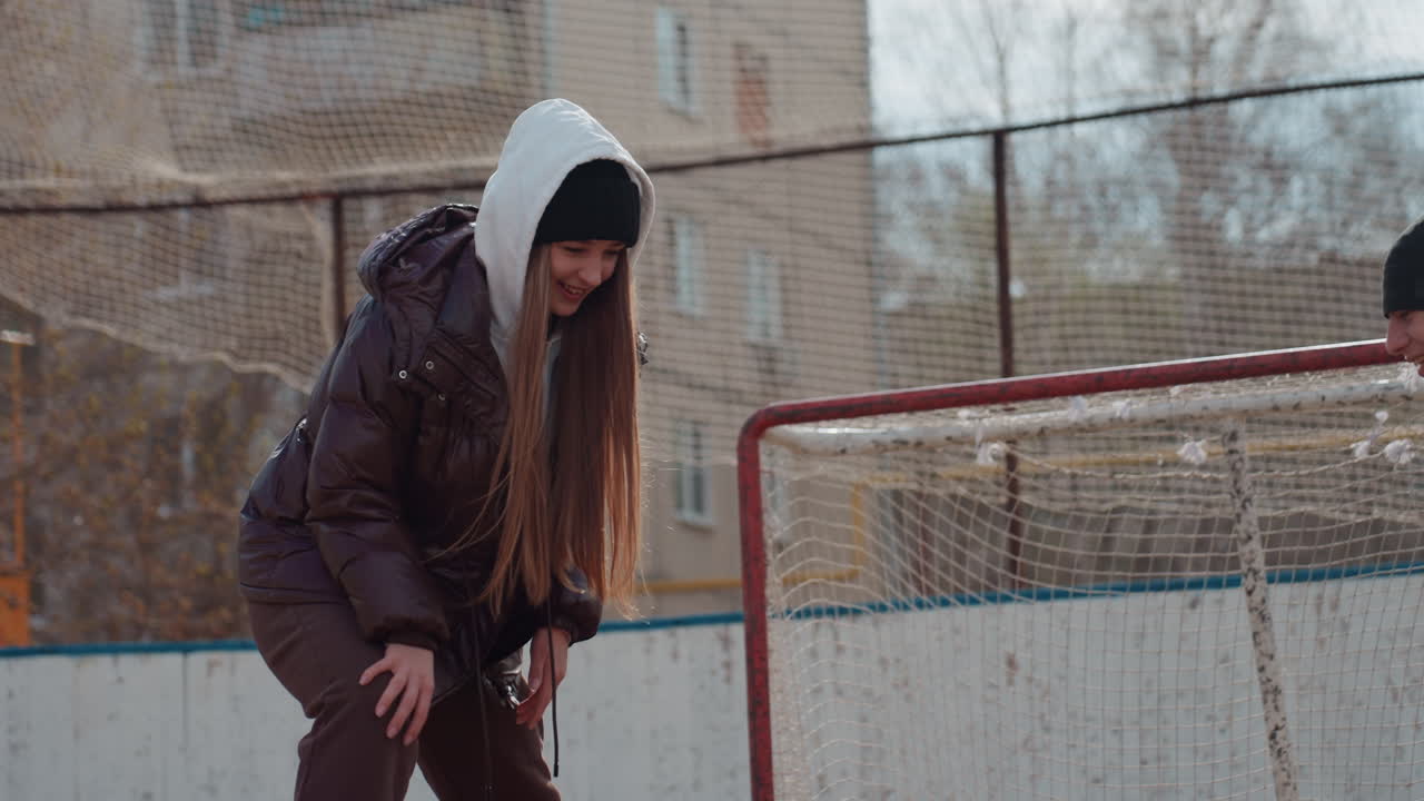 young caucasian goalkeeper practicing saves at goal, low crouch and quick movement, hoodie up and focused gaze, urban rink backdrop, playful drill with energetic rhythm and reflex training