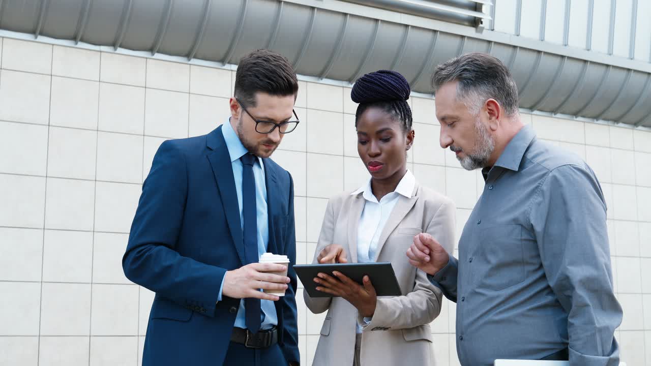 Close-up view of african american businesswoman and two caucasian businessmen reading something on the tablet and talking in the street