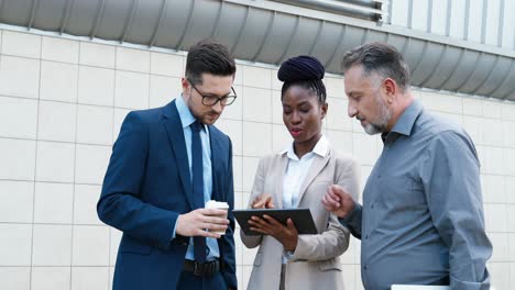 close-up view of african american businesswoman and two caucasian businessmen reading something on the tablet and talking in the street