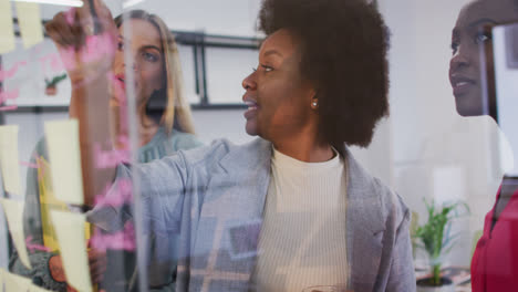 Drei-Unterschiedliche-Geschäftsfrauen-Machen-Ein-Brainstorming-Und-Schreiben-Memonotizen-An-Einer-Glaswand-Im-Büro