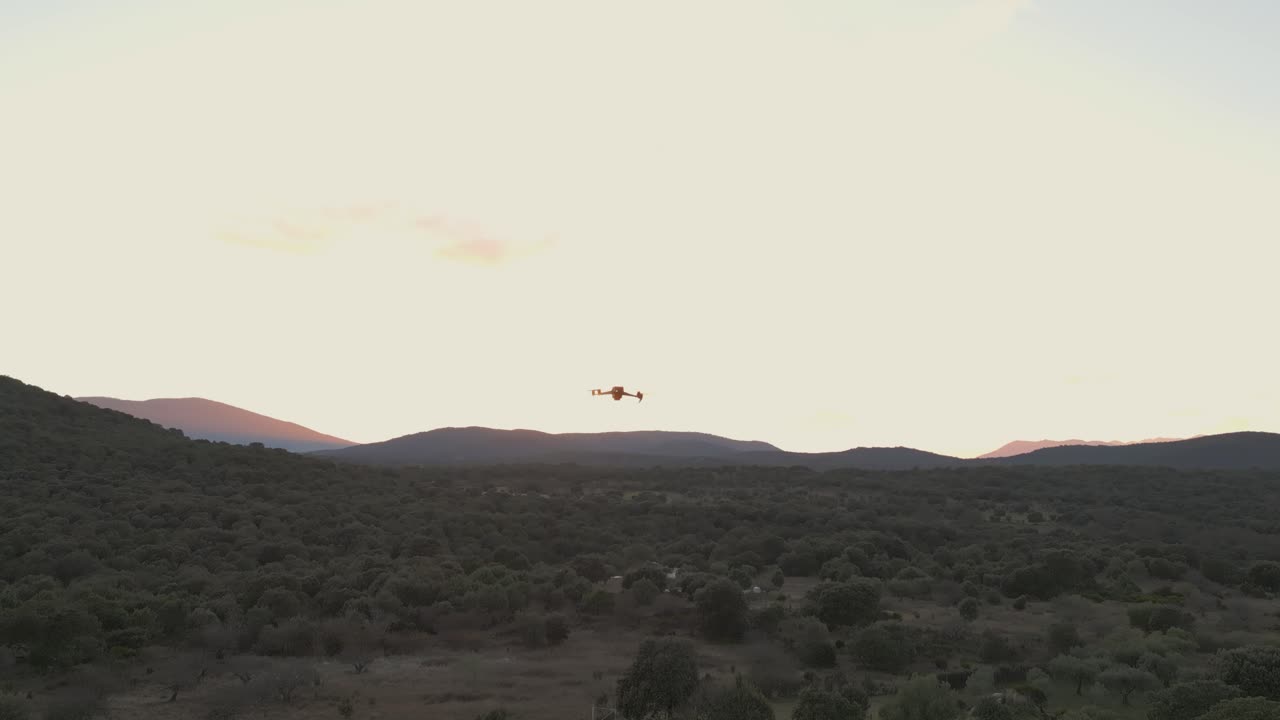 Filmato al rallentatore di un drone che scende in una valle al tramonto, mostrando un cielo dalle tonalità gialle mentre le luci del drone rimangono visibili mentre si muove verso la vegetazione più scura sottostante