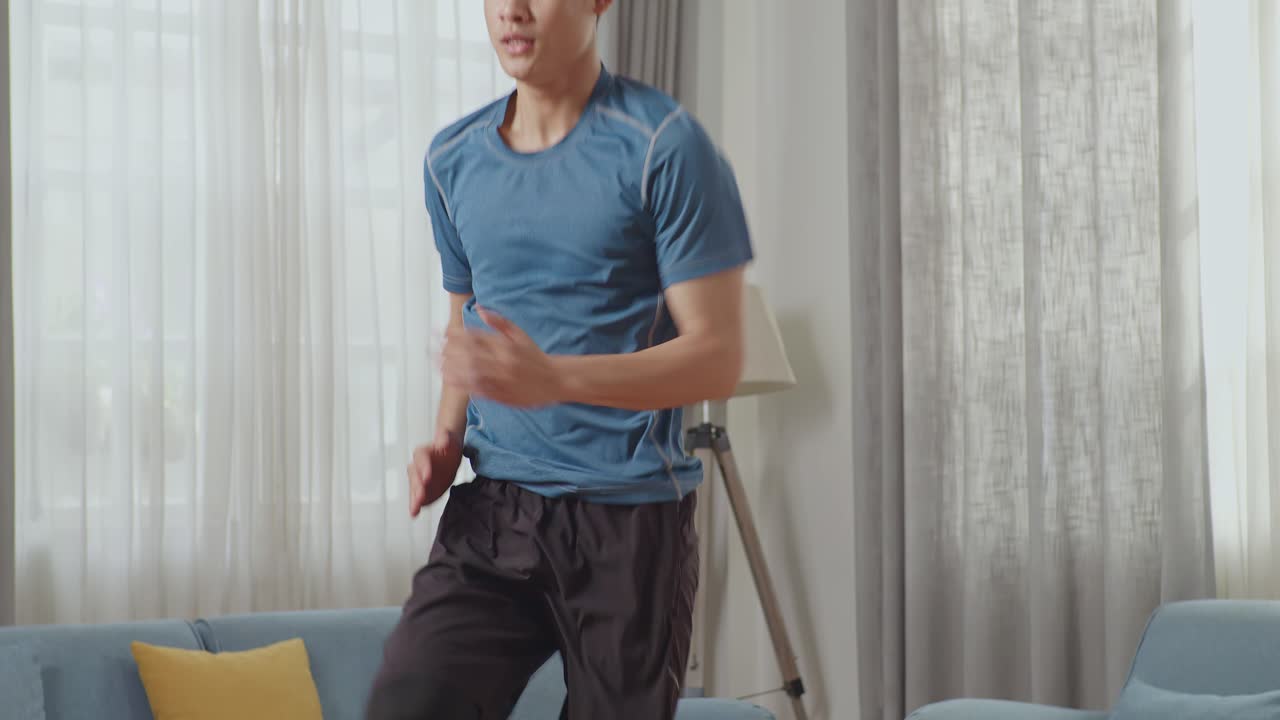 스포츠 옷을 입은 아시아 운동 피트니스 남자가 현대적인 인테리어가 있는 거실에서 활기차게 조하고 있습니다.