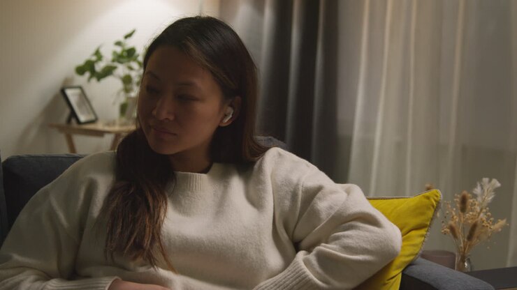 Woman Spending Evening At Home On Sofa Wearing Wireless Earbuds And Streaming Music Or Podcast 1