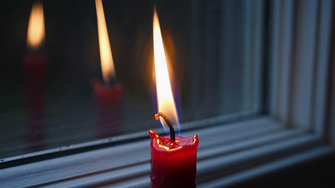 Close-up of a red candle flame reflecting in a window, shot at eye level