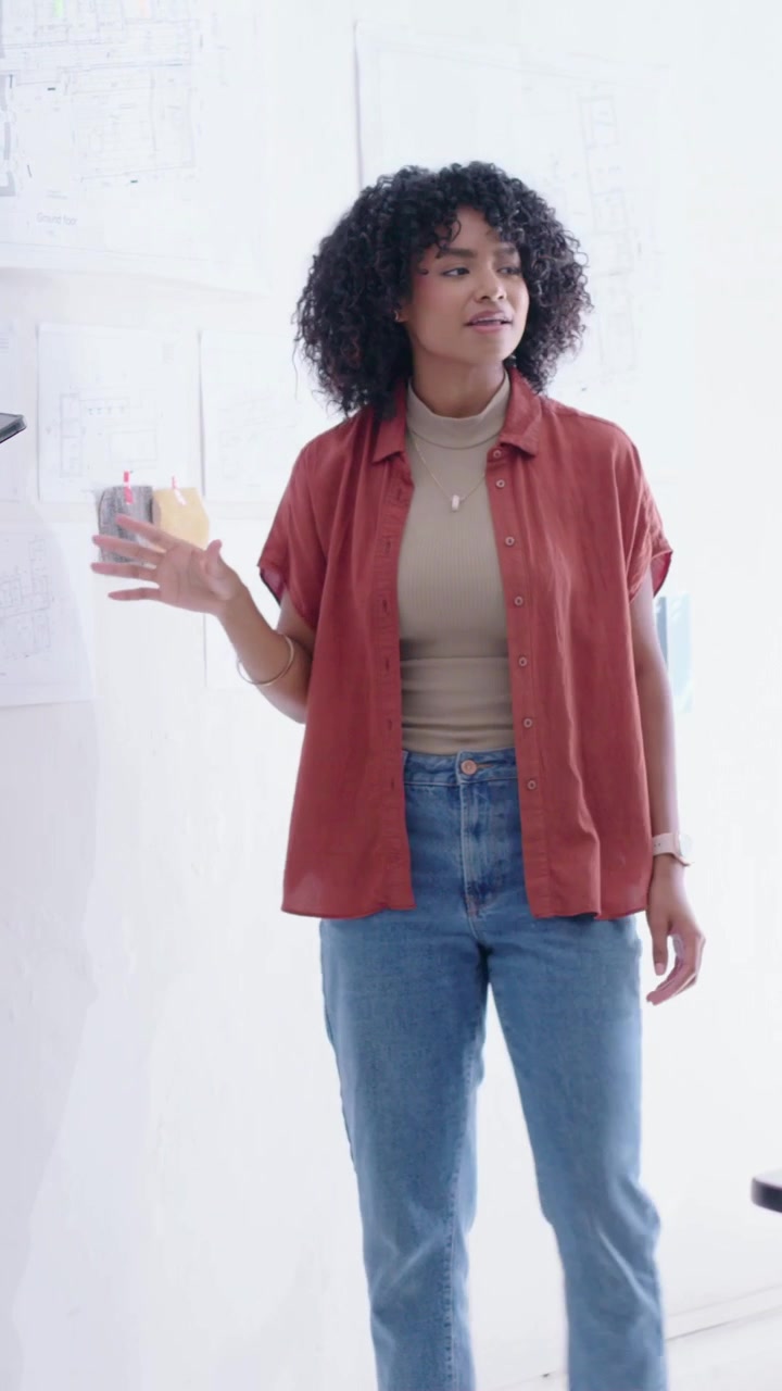 Video verticale: Donna con camicia color ruggine che sistema post-it sul muro, organizzando il layout.