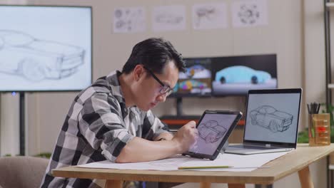 side view of asian male drawing new car design concept on a tablet following by a laptop in the studio with tv and computers display 3d electric car model