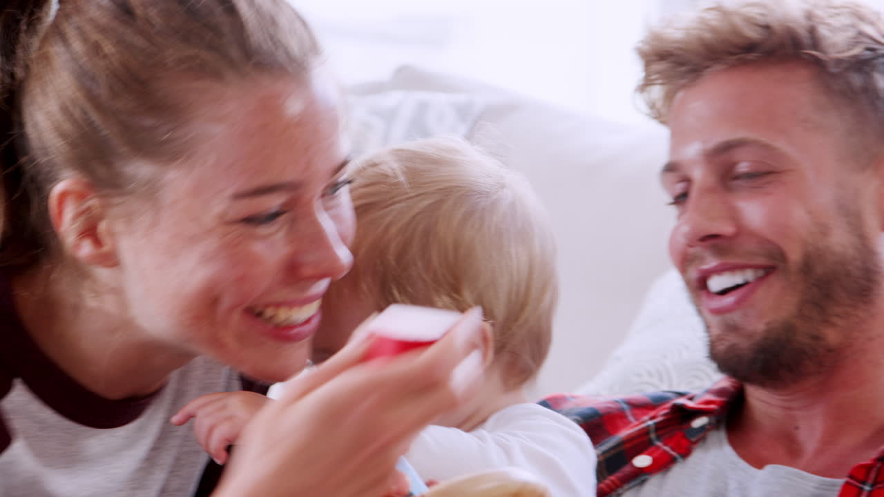 젊은 백인 부부는 거실에서 그들의 유아와 함께 놀고 있습니다.