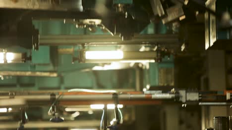 in an industrial environment, rows of robotic arms, adorned with suction cups, extend from ceiling-mounted metal frameworks, with blurred stacks of metal cans visible in the backdrop