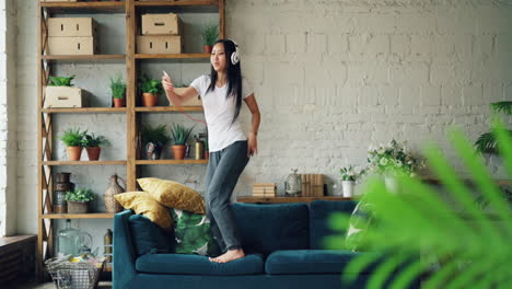 woman dancing on a sofa with headphones
