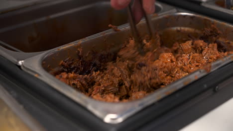 Cook-stirs-chopped-beef-with-tongs-in-commercial-restaurant-kitchen