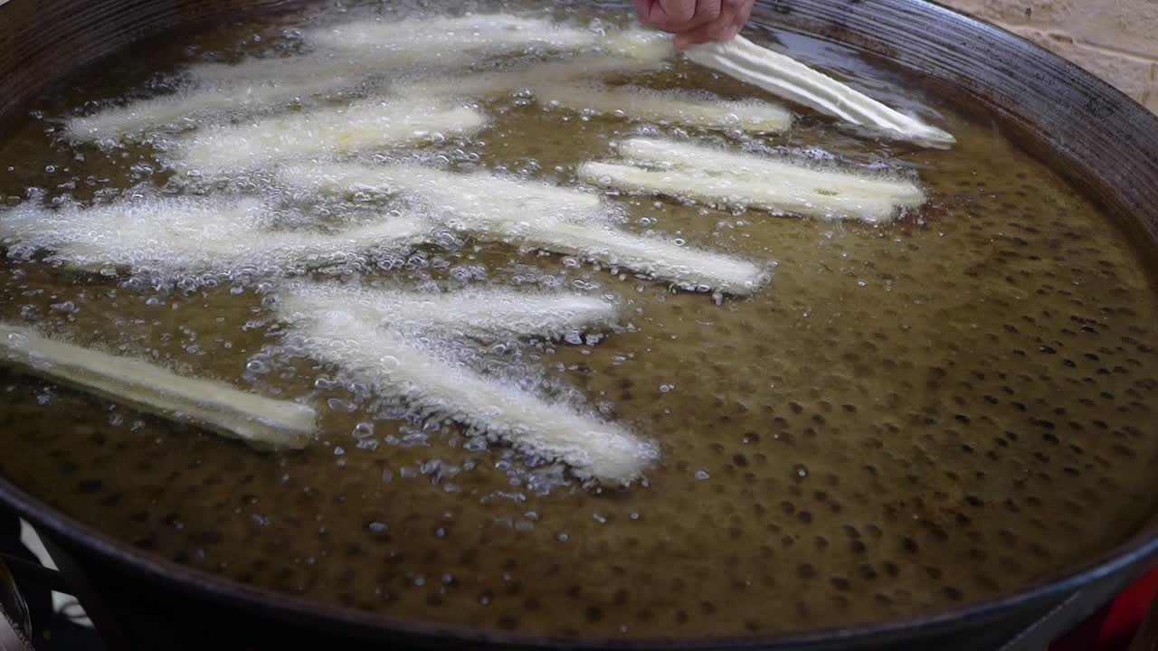 Closeup of churros being placed in boiling oil for cooking.