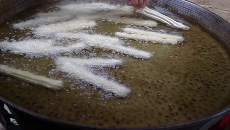closeup of churros being placed in boiling oil for cooking.