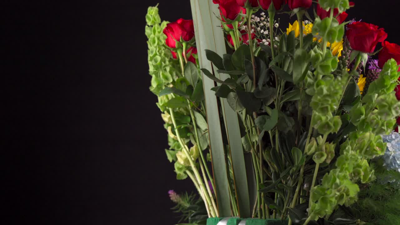 Composizione floreale con rose, margherite, gigli e gerbere che ruotano e scorrono su sfondo nero.