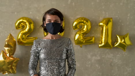 new year and covid-19. young pretty woman puts on face mask on new year's eve. front view. female wearing evening dress at glamorous party.