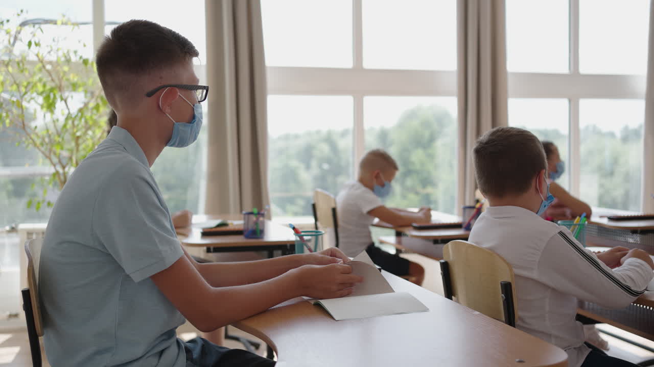 학교에서 마스크를 쓰고 교실에 있는 아이들은 교실에 앉아서 스로우 모션으로 손을 들어 선생님의 질문에 대답합니다. 학교에서 전염병 기간 동안의 수업