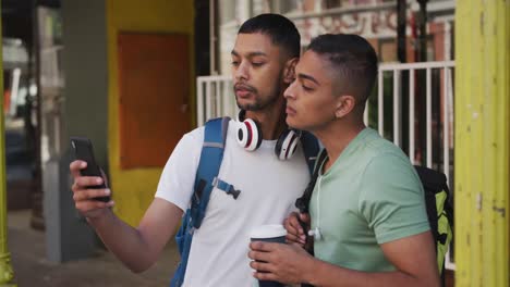 dos amigos varones de raza mixta bebiendo café y usando un teléfono inteligente en la calle