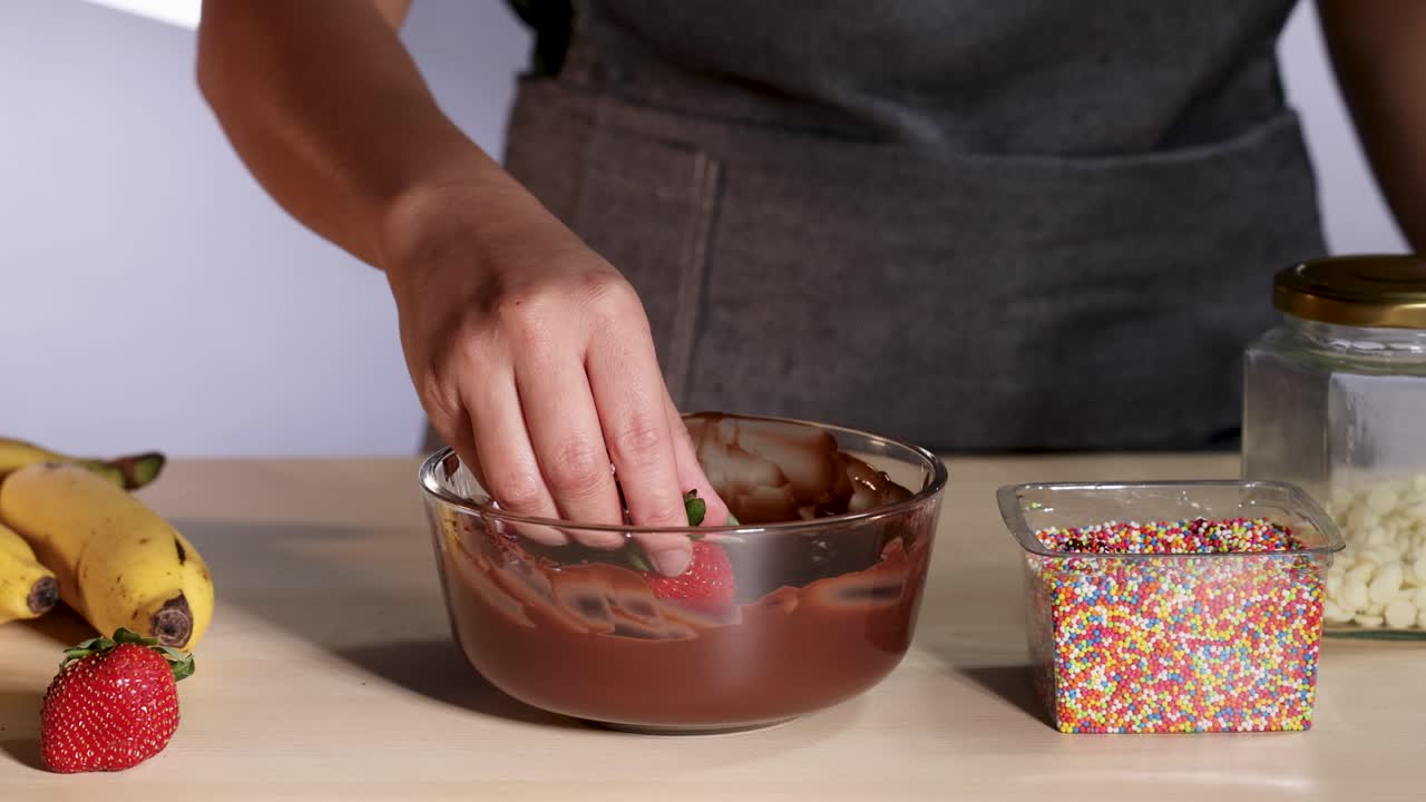 persona sumergiendo fresa en chocolate y salpicaduras de colores