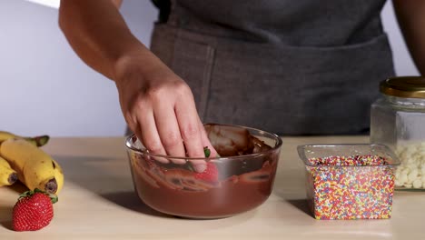 person dipping strawberry in chocolate and colorful sprinkles