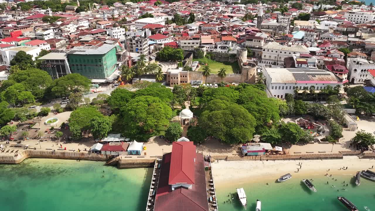 Ripresa aerea cinematografica con drone sopra i Forodhani Gardens e il Forte Vecchio a Stone Town, Zanzibar. Il parco di fronte all'oceano, la storica architettura swahili e la vivace vita costiera creano una scena di viaggio mozzafiato