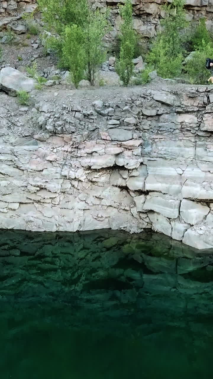 Clean water background near the stone slope and the tourist walking on it. Aerial filming of a rocky canyon with a wanderer outdoors. Motion bottom up Vertical video