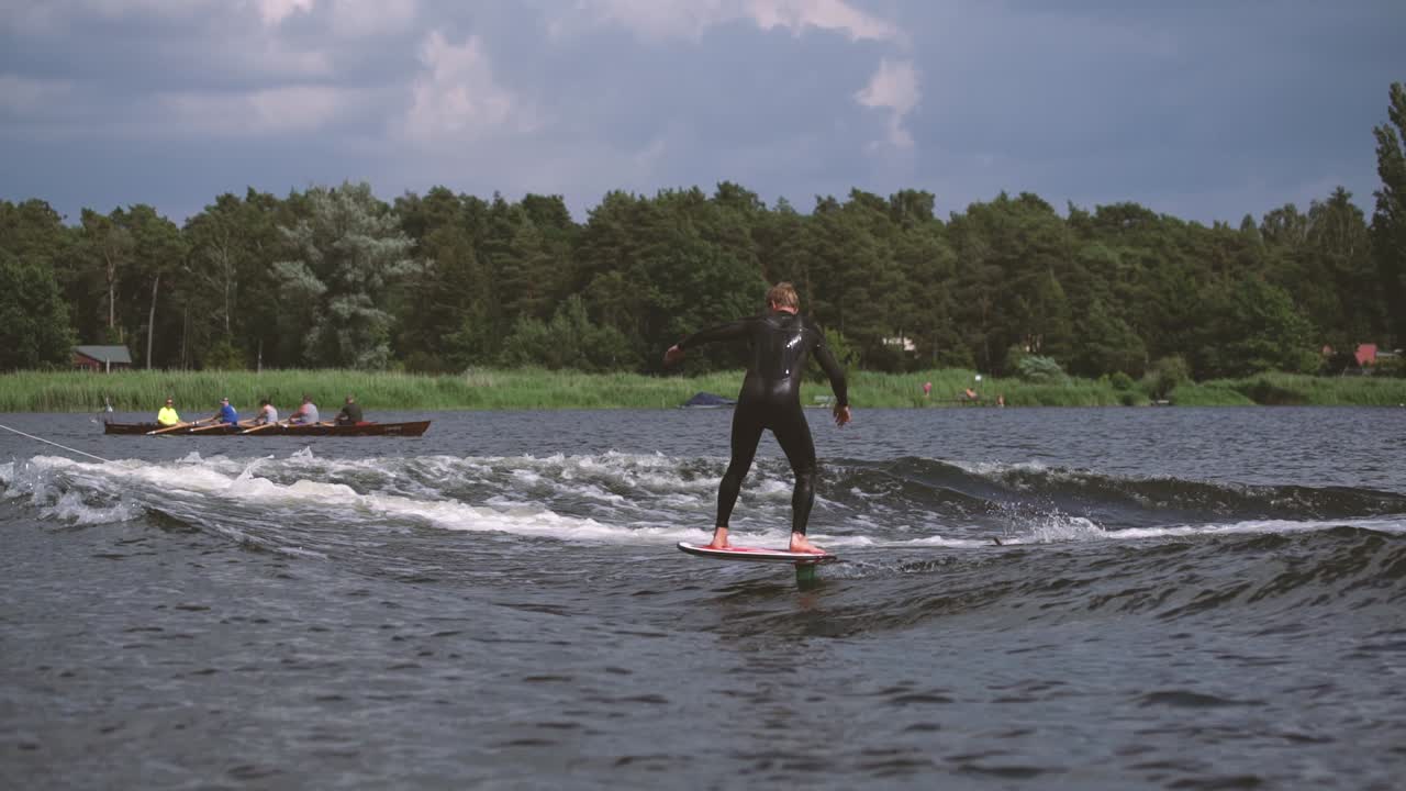 мужчина на рапире серфит на волне с гребцом на заднем плане