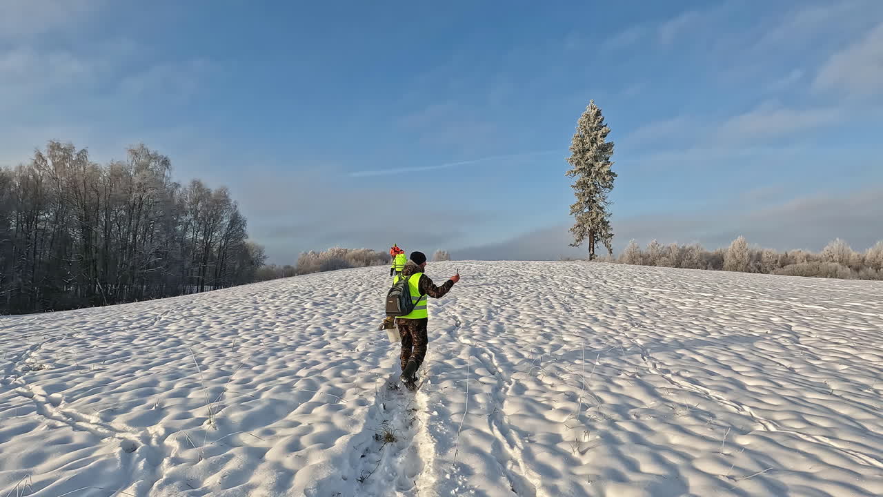 hombre en chaleco reflectante tomando video con cámara de teléfono inteligente mientras camina sobre la nieve en un día de invierno