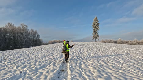 hombre en chaleco reflectante tomando video con cámara de teléfono inteligente mientras camina sobre la nieve en un día de invierno