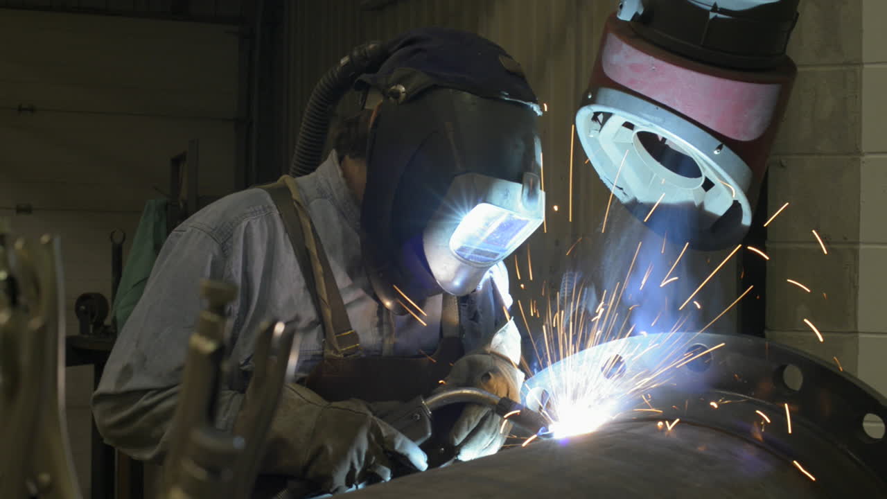 Sparks fly as a man welds a large pipe in an industrial machine shop