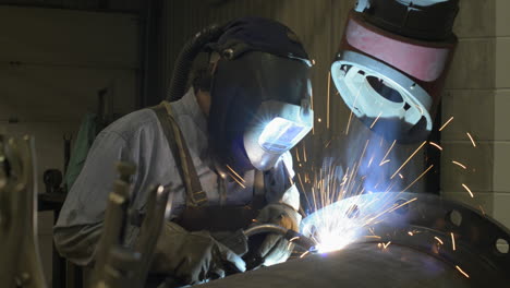 sparks fly as a man welds a large pipe in an industrial machine shop