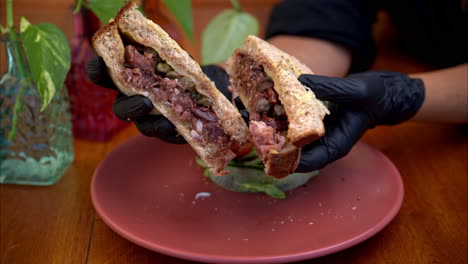 slow motion of a person wearing black latex gloves holding and presenting a prosciutto with fig sauce and capers sandwich