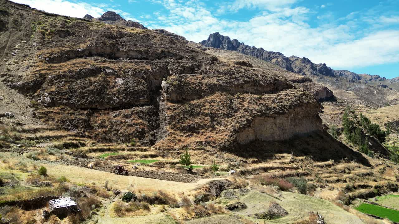 Drone footage revealing the harmony of past and present — a farmer in a red tractor works golden Andean fields encircled by ancient stepped terraces
