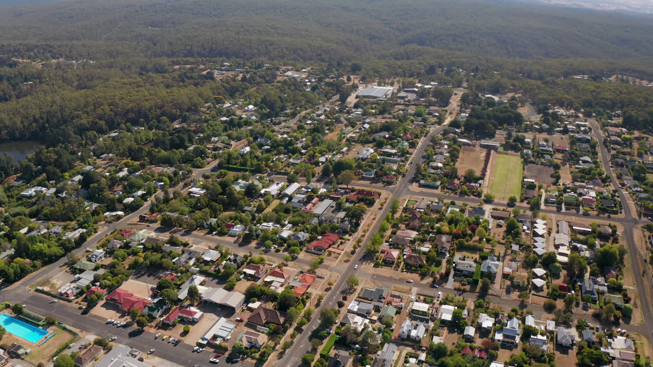 toma aérea hacia atrás de la ciudad de daylesford con carreteras, lago y hermosas colinas rurales en el fondo