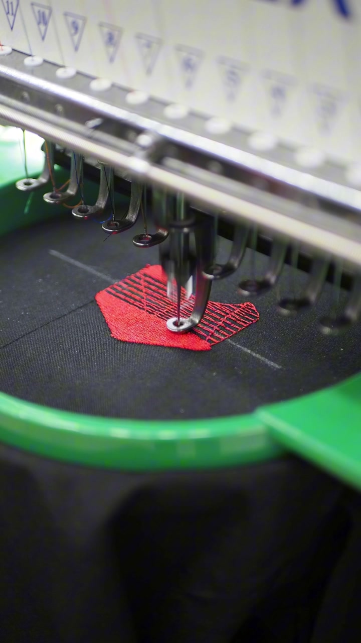 Macchina da ricamo industriale che ricama un disegno rosso su tessuto nero