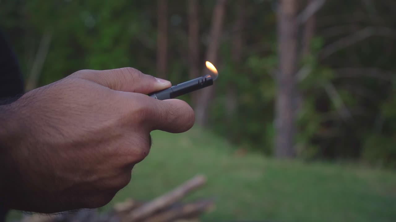 Slow-motion close-up shot of a hand starting a lighter outside in nature, capturing the moment as the flame ignites