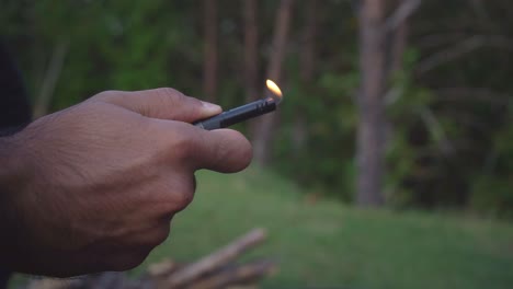slow-motion close-up shot of a hand starting a lighter outside in nature, capturing the moment as the flame ignites