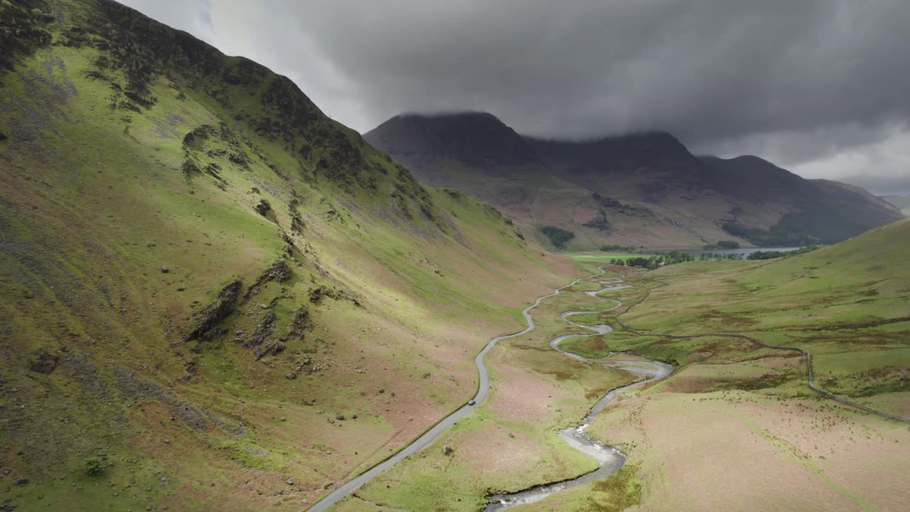 Un'auto in lontananza attraversa una vasta valle nel Lake District inglese, con nuvole minacciose in cielo in una giornata coperta