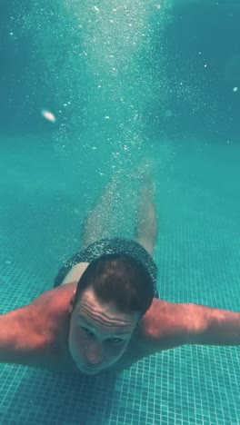 young guy swims underwater in a swimming pool