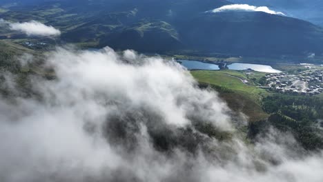 Volando-A-Través-De-Las-Nubes-Y-La-Niebla-Atmosférica-Temprano-En-La-Mañana-Con-Rayos-De-Sol-Brillando-A-Través-Del-Cielo-Y-Lagos-En-El-Fondo-Montañoso-En-La-Plataforma-Aérea-De-Colorado