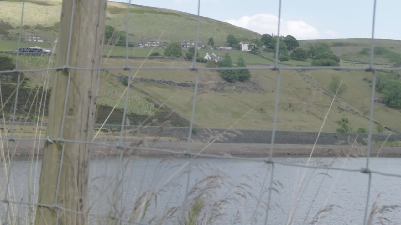 View of Butterley reservoir and Yorkshire hills wide tilting shot through fence