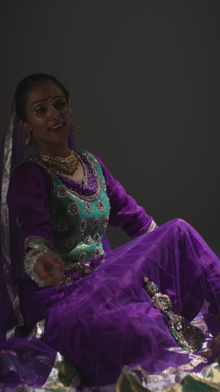 video vertical de una bailarina de kathak que realiza un baile vestida con un vestido tradicional indio sentada en el suelo en el centro de atención 1