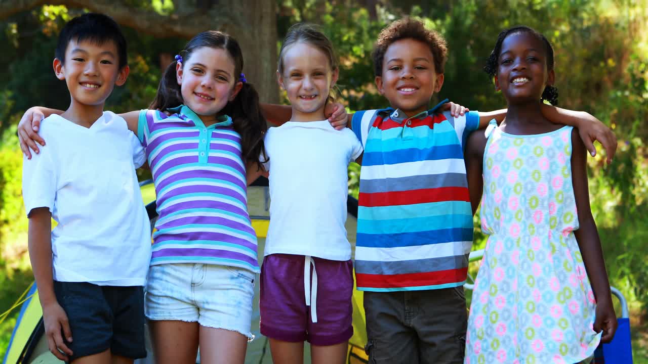 Kids standing with arms around outside tent at campsite