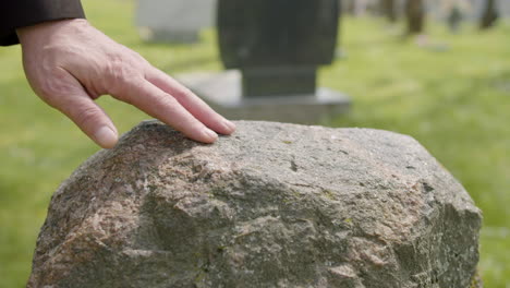 close up view of man hand touching a tombstone in a graveyard