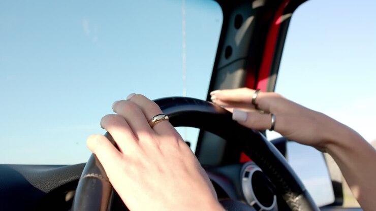 Mani di giovane donna sul volante che guida un'auto in una giornata di sole