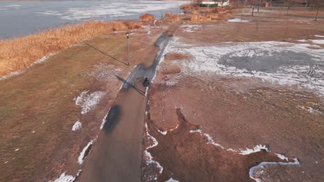aerial footage captures a man running in freezing conditions, skillfully avoiding frozen puddles scattered along his path. the high-angle view emphasizes the harsh winter environment.