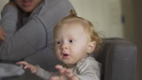 toddler sitting at the dining table while drinking milk from her bottle, sitting next to mom